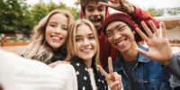 Group if cheerful multiethnic friends teenagers spending fun time together outdoors, taking a selfie